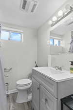 Full bath with wood finished floors, vanity, a textured wall, plenty of natural light, and a textured ceiling