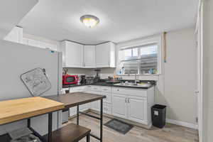Kitchen featuring freestanding refrigerator, dark countertops, white cabinetry, light wood finished floors, and a textured ceiling