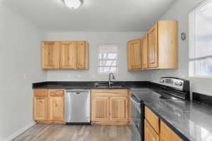 Kitchen featuring appliances with stainless steel finishes, light wood-style floors, dark stone counters, and light brown cabinets