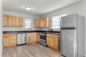 Kitchen featuring appliances with stainless steel finishes, light wood-style floors, healthy amount of natural light, and dark stone counters