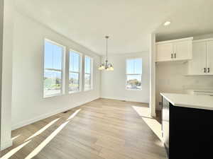 Kitchen featuring white cabinetry, light wood-style flooring, hanging light fixtures, dark cabinets, and a chandelier