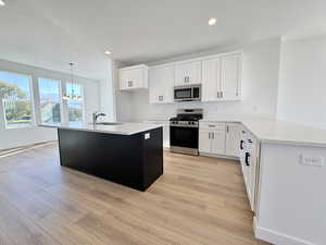 Kitchen with white cabinets, stainless steel appliances, dark cabinetry, a center island with sink, and recessed lighting