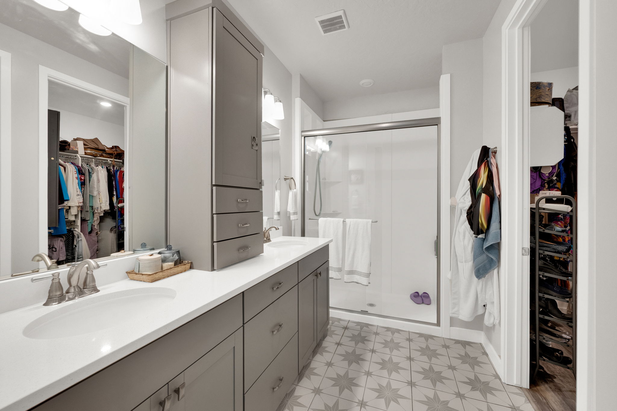 Bathroom with a walk in closet, light floors, double vanity, and a stall shower