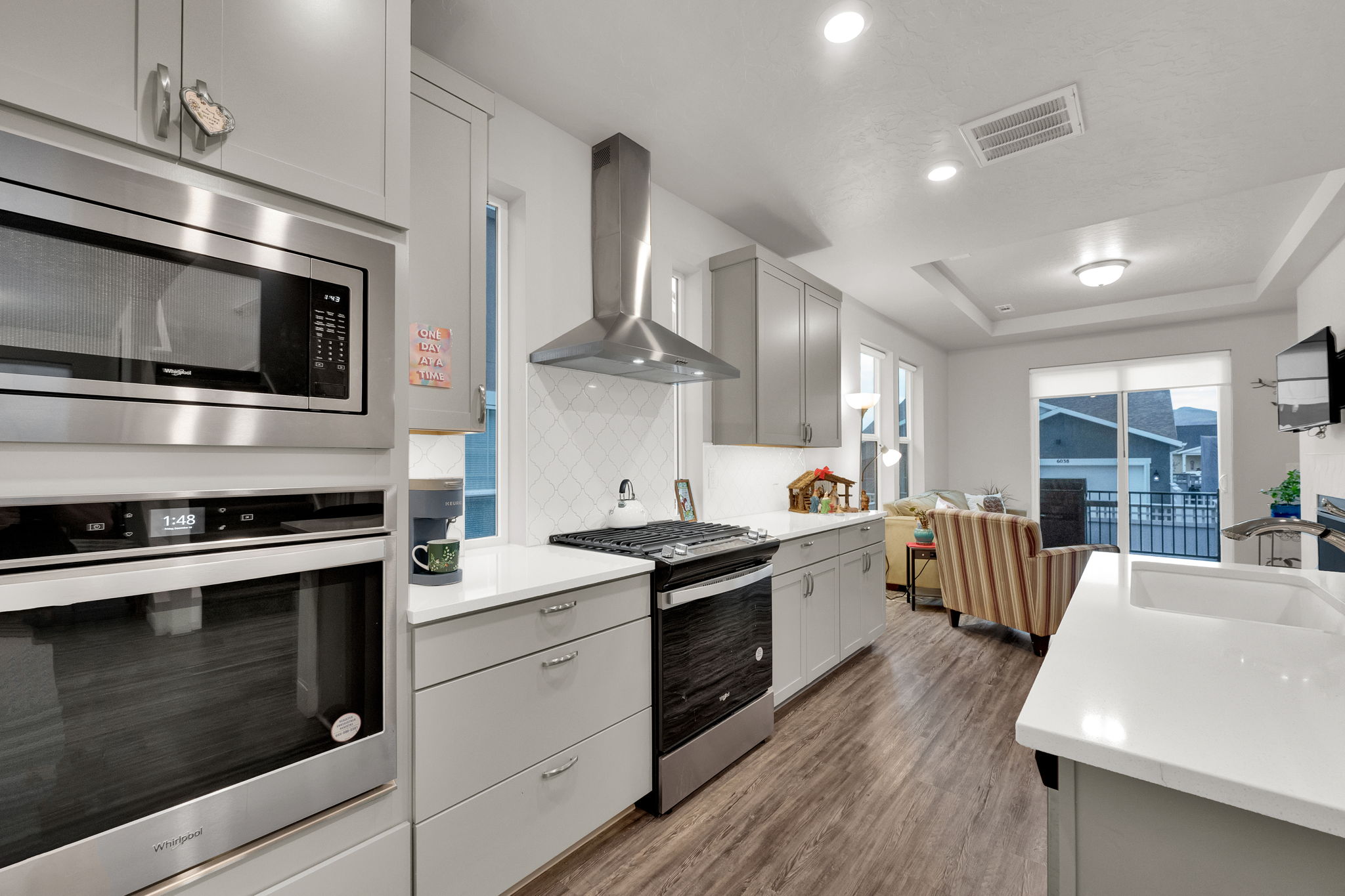 Kitchen with appliances with stainless steel finishes, gray cabinets, wall chimney exhaust hood, dark wood-type flooring, and recessed lighting