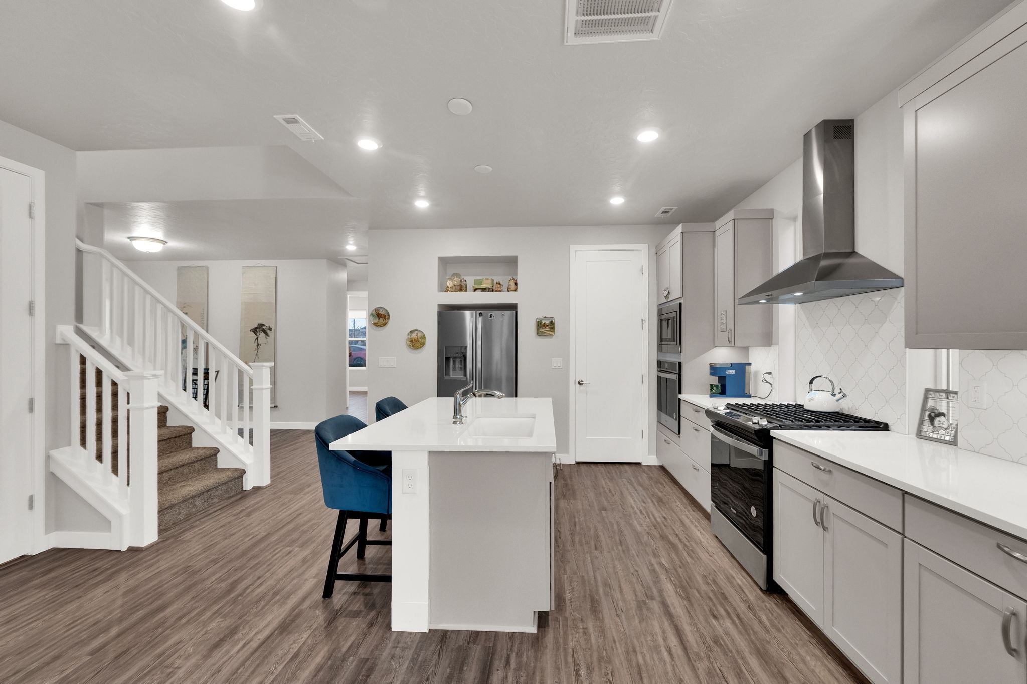 Kitchen featuring appliances with stainless steel finishes, wall chimney exhaust hood, a kitchen bar, gray cabinetry, and a center island with sink