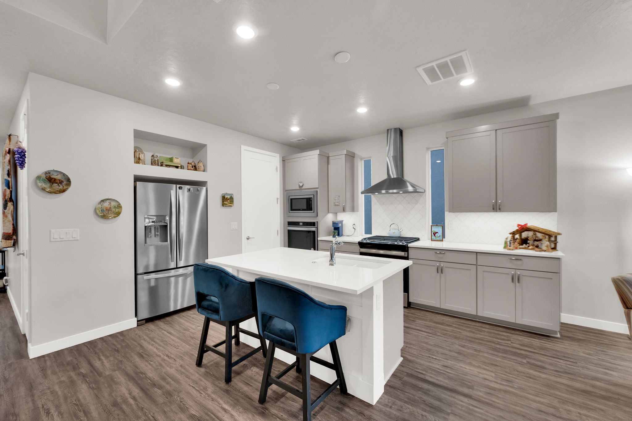 Kitchen featuring wall chimney range hood, a breakfast bar area, gray cabinets, appliances with stainless steel finishes, and an island with sink