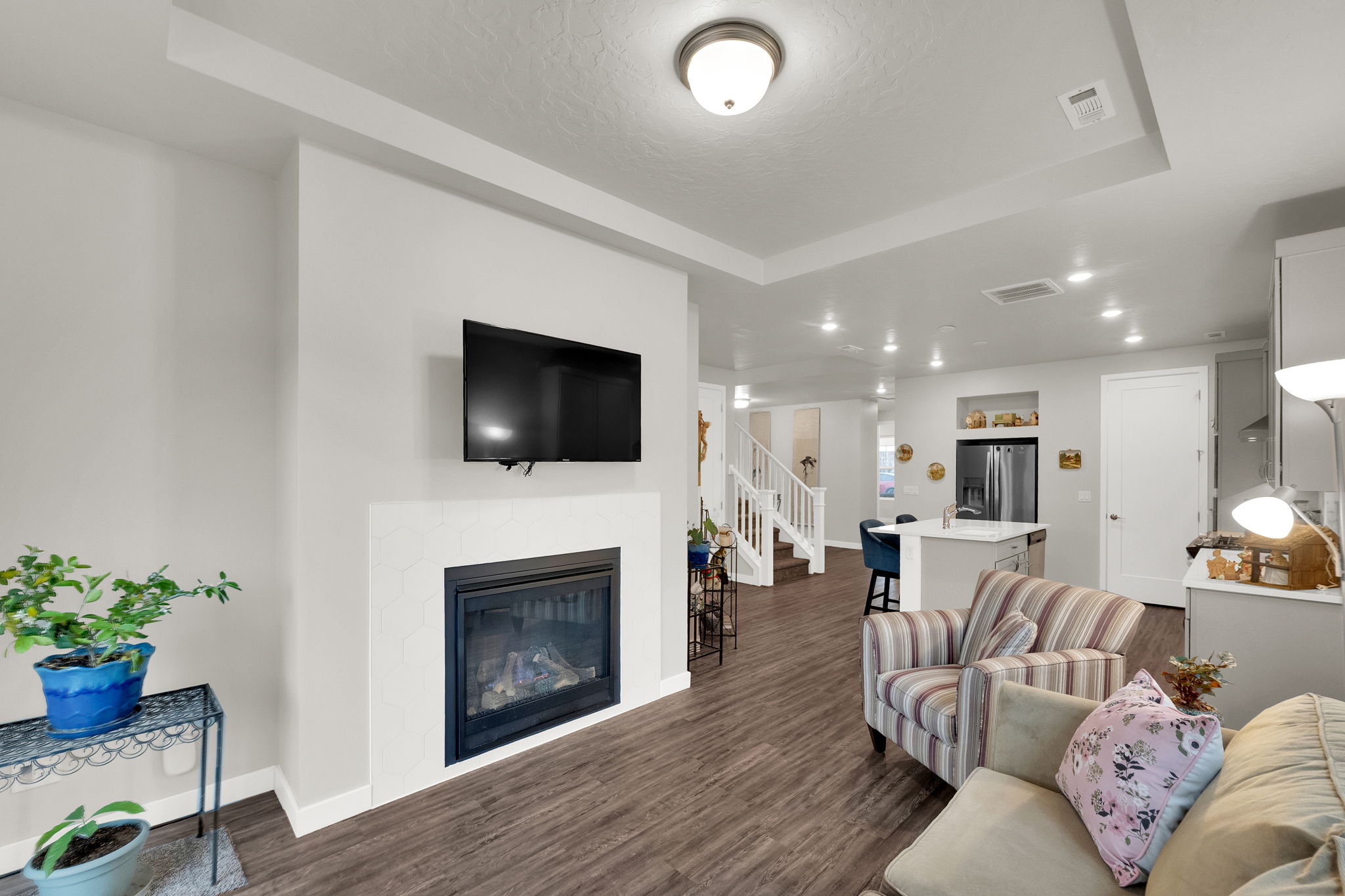 Living room featuring a glass covered fireplace, recessed lighting, stairway, dark wood-type flooring, and a raised ceiling