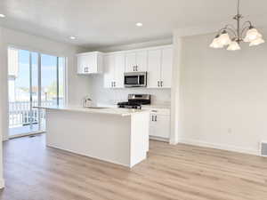 Kitchen with hanging light fixtures, white cabinets, stainless steel appliances, a kitchen island with sink, and light wood-style floors