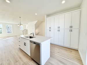 Kitchen featuring white cabinets, pendant lighting, dishwasher, light wood-style flooring, and a kitchen island with sink