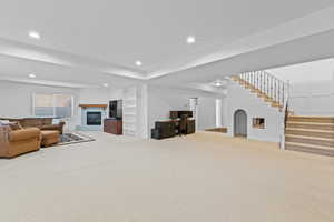Living room featuring an office area, light colored carpet, a glass covered fireplace, recessed lighting, and stairs