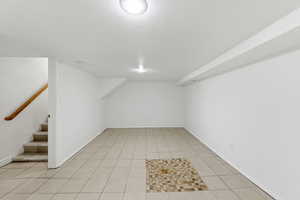 Finished basement featuring stairway, a textured ceiling, and light tile patterned floors