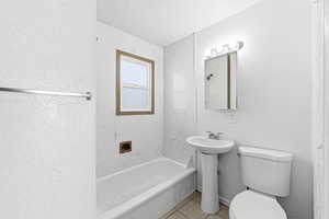 Full bathroom with a textured ceiling, shower / tub combination, light tile patterned floors, and a textured wall