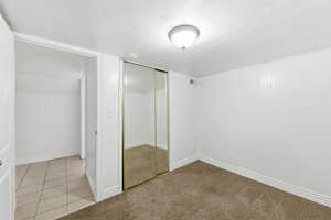 Unfurnished bedroom featuring light colored carpet, a closet, light tile patterned flooring, and a textured ceiling