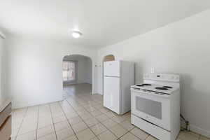 Kitchen featuring white appliances, arched walkways, light tile patterned flooring, and light countertops