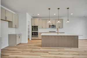 Kitchen featuring cream cabinets, hanging light fixtures, stainless steel appliances, light wood finished floors, and light stone countertops