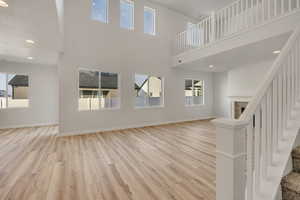 Unfurnished living room featuring recessed lighting, light wood-style flooring, a tiled fireplace, stairs, and a towering ceiling