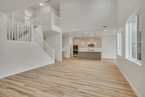 Unfurnished living room featuring stairway, light wood-style flooring, a towering ceiling, and recessed lighting