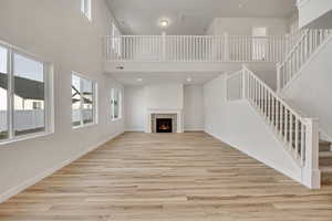 Unfurnished living room featuring stairs, a tile fireplace, light wood finished floors, healthy amount of natural light, and a towering ceiling