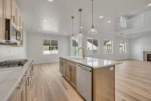 Kitchen with open floor plan, appliances with stainless steel finishes, light wood-style floors, light stone countertops, and decorative light fixtures