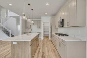 Kitchen featuring decorative light fixtures, a kitchen island with sink, light wood finished floors, light stone countertops, and appliances with stainless steel finishes