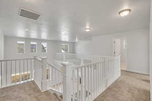 Corridor with light carpet, an upstairs landing, and a textured ceiling