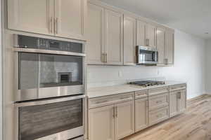 Kitchen featuring stainless steel appliances, light wood finished floors, light stone countertops, and cream cabinetry