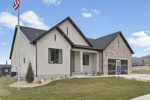 View of front of property featuring a front yard, stucco siding, covered porch, stone siding, and a shingled roof