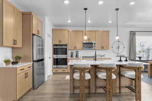 Kitchen with hanging light fixtures, light brown cabinets, light stone counters, appliances with stainless steel finishes, and recessed lighting