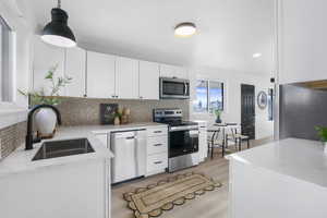 Kitchen featuring white cabinets, appliances with stainless steel finishes, pendant lighting, light wood-style floors, and light stone countertops