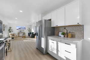 Kitchen with white cabinetry, open floor plan, tasteful backsplash, light wood-style floors, and appliances with stainless steel finishes