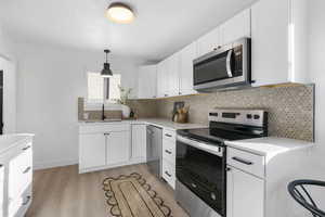 Kitchen featuring stainless steel appliances, white cabinetry, pendant lighting, and light wood-type flooring