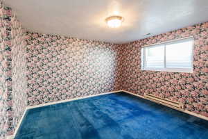 Carpeted empty room featuring a textured ceiling, a baseboard radiator, and wallpapered walls