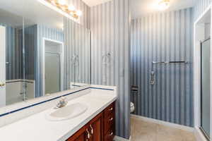Bathroom featuring wallpapered walls, light tile patterned floors, vanity, and a stall shower