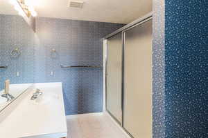 Bathroom featuring wallpapered walls, vanity, a stall shower, light tile patterned flooring, and a textured ceiling