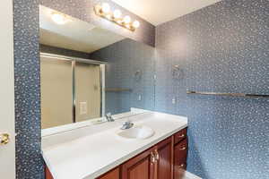 Full bath featuring wallpapered walls, vanity, and a shower stall