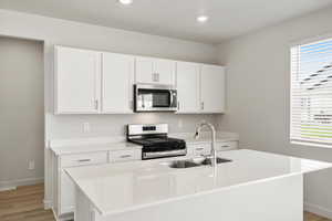 Kitchen with stainless steel appliances, white cabinets, light stone countertops, and an island with sink