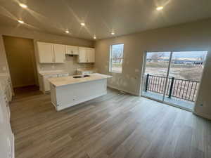 Kitchen featuring white cabinetry, recessed lighting, light wood-style flooring, a center island, and light stone countertops