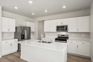 Kitchen featuring stainless steel appliances, an island with sink, white cabinetry, light stone counters, and recessed lighting