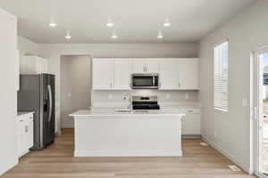 Kitchen featuring white cabinetry, appliances with stainless steel finishes, light wood-style floors, a kitchen island with sink, and recessed lighting