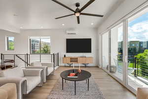 Living area with light wood-style flooring, ceiling fan, recessed lighting, and a wall mounted AC