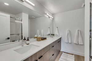 Full bath with double vanity, a stall shower, and light wood-style floors