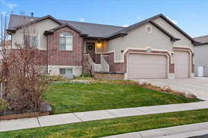 View of front facade with brick siding, a front lawn, an attached garage, stucco siding, and concrete driveway