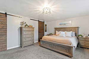 Bedroom featuring a barn door, a textured ceiling, and light colored carpet