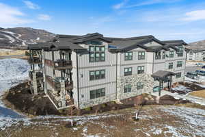 View of snowy exterior featuring stone siding, a mountain view, and board and batten siding