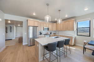 Kitchen with light brown cabinets, stainless steel appliances, light countertops, light wood-style flooring, and hanging light fixtures