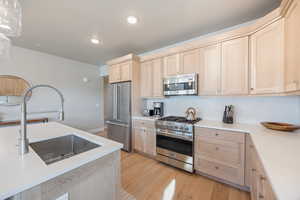 Kitchen with light brown cabinets, high end appliances, light wood finished floors, light stone counters, and recessed lighting