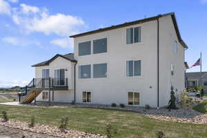 Rear view of property featuring a lawn, stairway, a deck, and stucco siding