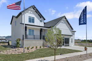 Modern farmhouse featuring board and batten siding, a porch, a front lawn, driveway, and roof with shingles