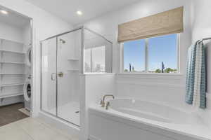 Bathroom featuring a bath, a stall shower, estacked washer and dryer, recessed lighting, and a spacious closet
