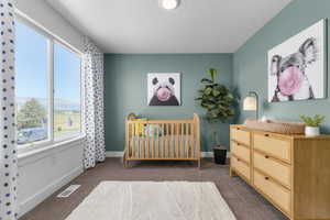 Bedroom featuring a nursery area, carpet, and a textured ceiling